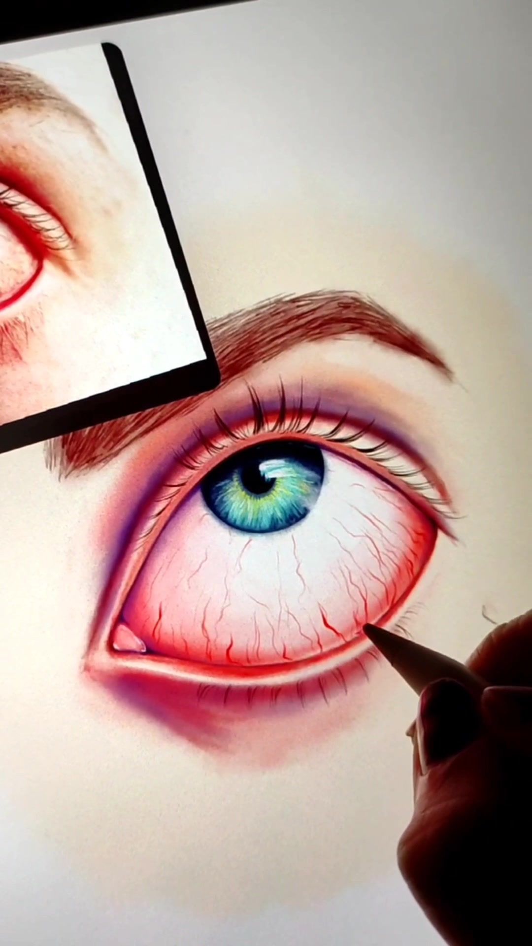 Ilustración digital de un ojo enrojecido, con venitas y el iris azul verdoso, en la pantalla de una tableta. En una esquina, la foto de referencia; abajo, la punta del lápiz digital.